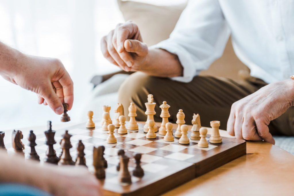 Selective focus of wooden chess board with seniors playing chess at home e1697916079176.jpg